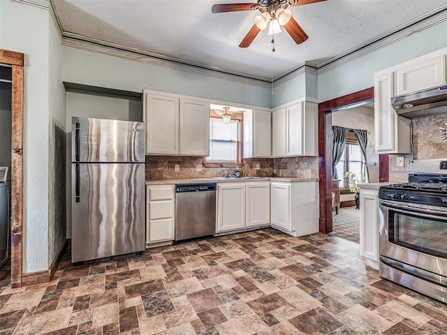 kitchen with white cabinetry, ornamental molding, appliances with stainless steel finishes, range hood, and backsplash