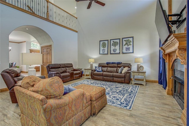 living room featuring ornamental molding, a towering ceiling, ceiling fan, and light hardwood / wood-style flooring