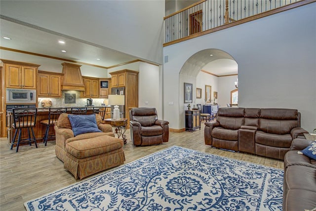 living room with crown molding, a towering ceiling, and light hardwood / wood-style floors