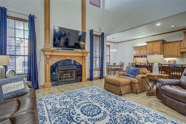 living room featuring crown molding, a chandelier, a fireplace, and light hardwood / wood-style flooring