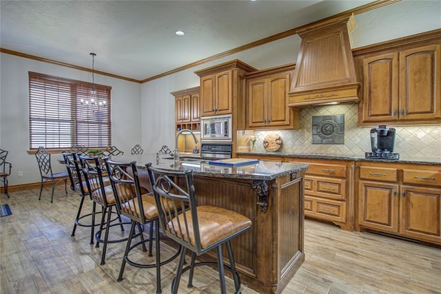 kitchen featuring a breakfast bar area, premium range hood, dark stone countertops, stainless steel appliances, and an island with sink