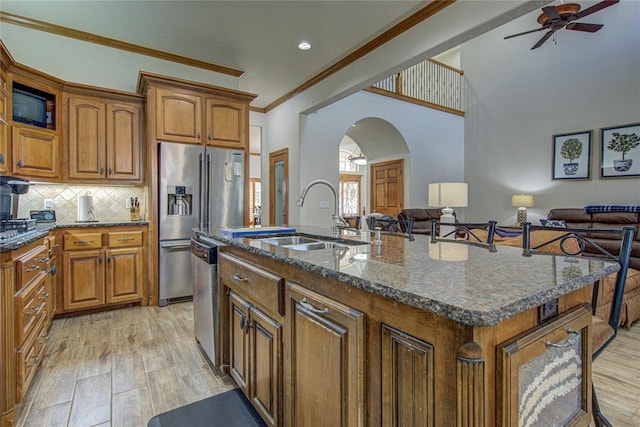 kitchen with sink, a kitchen island with sink, stainless steel appliances, tasteful backsplash, and light hardwood / wood-style floors