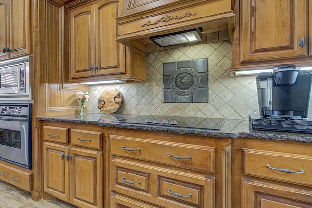 kitchen with stainless steel appliances, custom exhaust hood, decorative backsplash, and dark stone counters