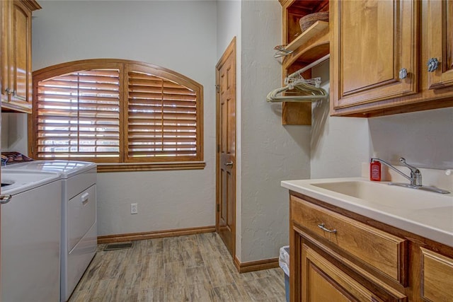 clothes washing area with sink, light hardwood / wood-style floors, cabinets, and washing machine and clothes dryer