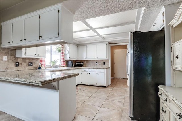 kitchen with sink, light stone counters, stainless steel refrigerator, kitchen peninsula, and white cabinets