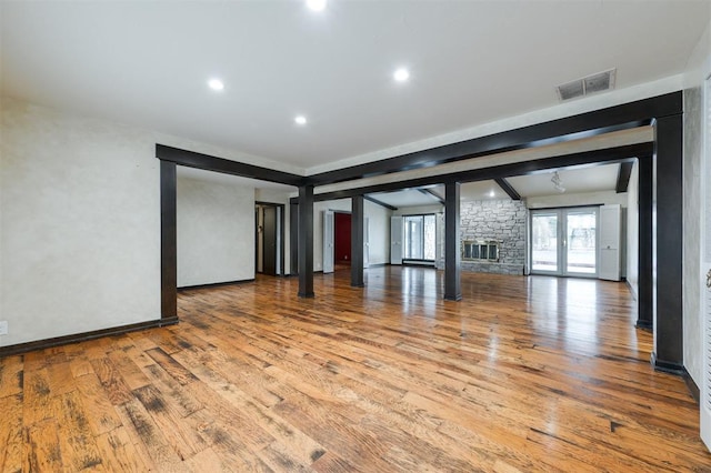 empty room featuring beamed ceiling, a stone fireplace, light hardwood / wood-style floors, and french doors