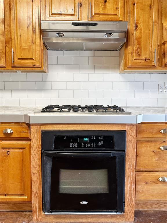 kitchen featuring stainless steel gas stovetop, decorative backsplash, oven, and range hood