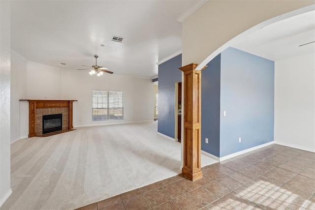 unfurnished living room with crown molding, a tile fireplace, ceiling fan, carpet floors, and ornate columns