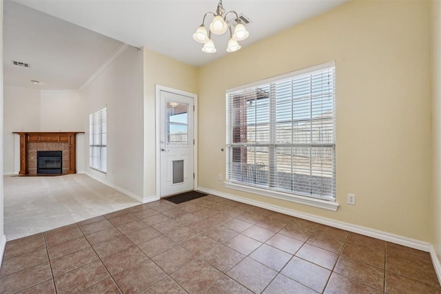 foyer entrance with a tiled fireplace, ornamental molding, tile patterned flooring, and a chandelier