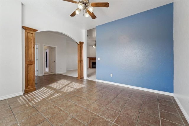 tiled empty room with a fireplace, decorative columns, and ceiling fan