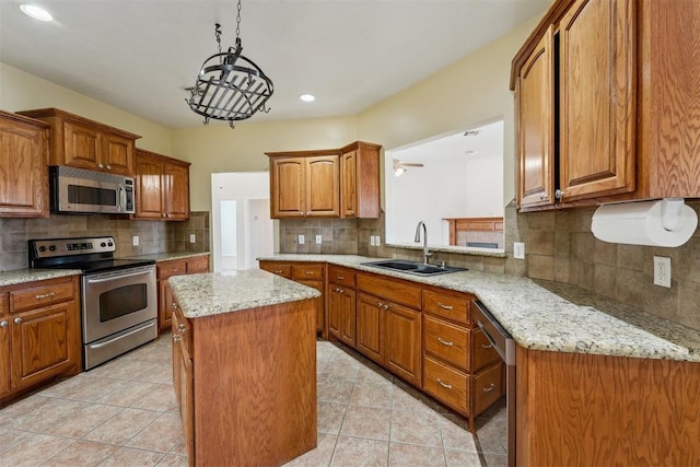 kitchen featuring sink, decorative light fixtures, appliances with stainless steel finishes, a kitchen island, and light stone countertops