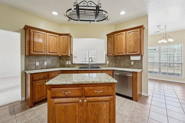 kitchen with sink, dishwasher, light stone counters, a kitchen island, and decorative light fixtures