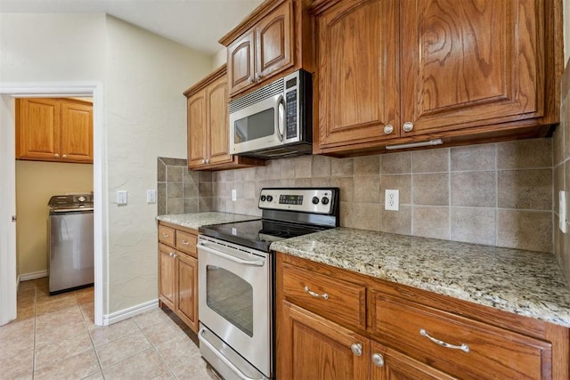 kitchen featuring appliances with stainless steel finishes, washer / clothes dryer, tasteful backsplash, light tile patterned floors, and light stone counters