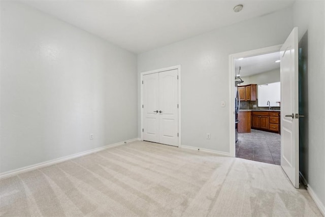 unfurnished bedroom with sink, a closet, light colored carpet, and stainless steel refrigerator