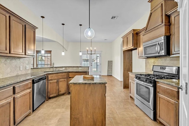 kitchen with sink, dark stone countertops, hanging light fixtures, stainless steel appliances, and a kitchen island