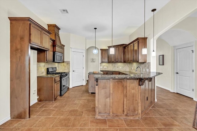 kitchen with a breakfast bar, hanging light fixtures, dark stone countertops, appliances with stainless steel finishes, and kitchen peninsula