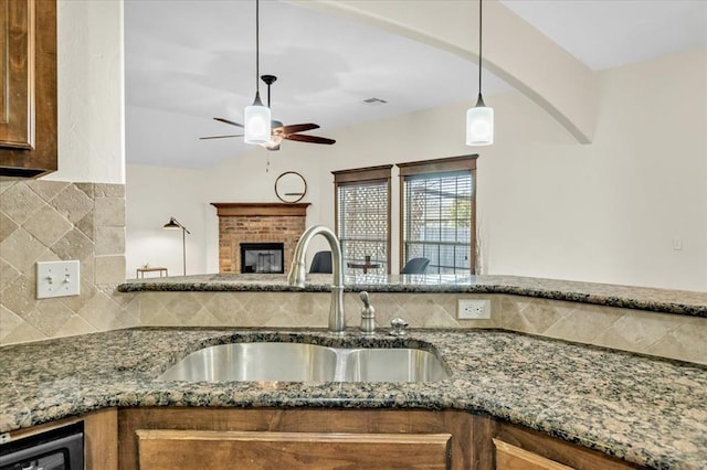 kitchen with stone counters, a fireplace, sink, decorative backsplash, and hanging light fixtures