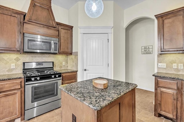 kitchen with a center island, light tile patterned floors, appliances with stainless steel finishes, dark stone counters, and backsplash