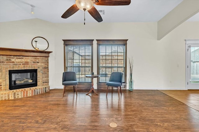 living area with hardwood / wood-style flooring, ceiling fan, vaulted ceiling, and a brick fireplace