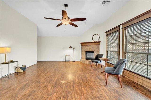 living area featuring vaulted ceiling, ceiling fan, hardwood / wood-style floors, and a brick fireplace