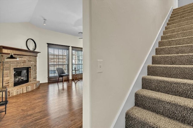 stairway featuring vaulted ceiling, hardwood / wood-style floors, and a fireplace