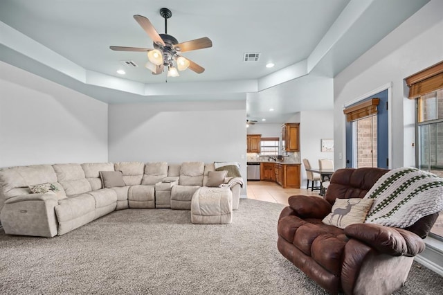 living room with ceiling fan, a tray ceiling, sink, and light tile patterned floors