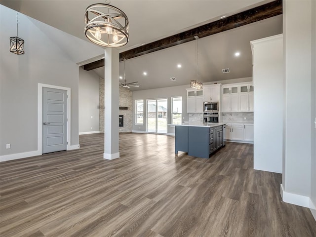 unfurnished living room featuring a stone fireplace, ceiling fan with notable chandelier, high vaulted ceiling, dark wood-type flooring, and beam ceiling