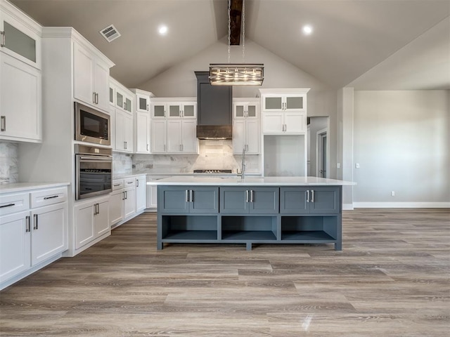 kitchen featuring tasteful backsplash, an island with sink, custom range hood, and stainless steel oven