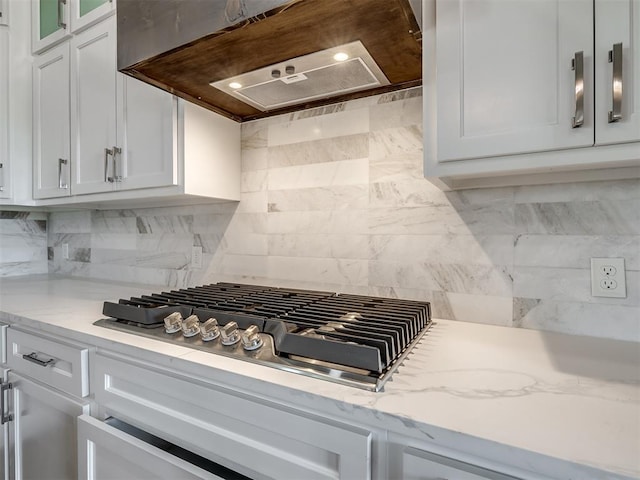 kitchen featuring tasteful backsplash, stainless steel gas stovetop, white cabinets, custom exhaust hood, and light stone countertops