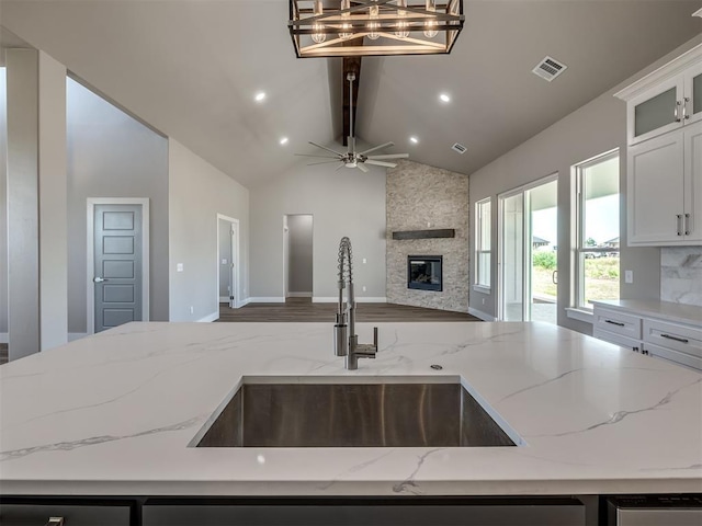 kitchen with lofted ceiling with beams, light stone counters, sink, and hanging light fixtures