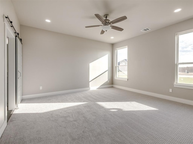 carpeted empty room featuring ceiling fan and a barn door