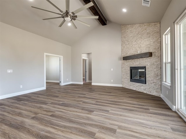 unfurnished living room with ceiling fan, hardwood / wood-style floors, beam ceiling, high vaulted ceiling, and a stone fireplace