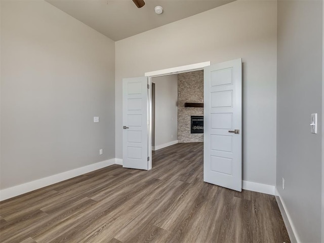 spare room featuring a fireplace, dark hardwood / wood-style floors, and ceiling fan