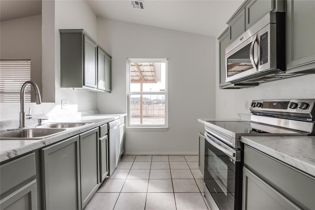 kitchen featuring gray cabinets, lofted ceiling, sink, light tile patterned floors, and stainless steel appliances