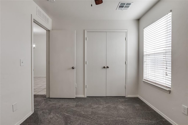 unfurnished bedroom featuring ceiling fan, a closet, multiple windows, and dark colored carpet