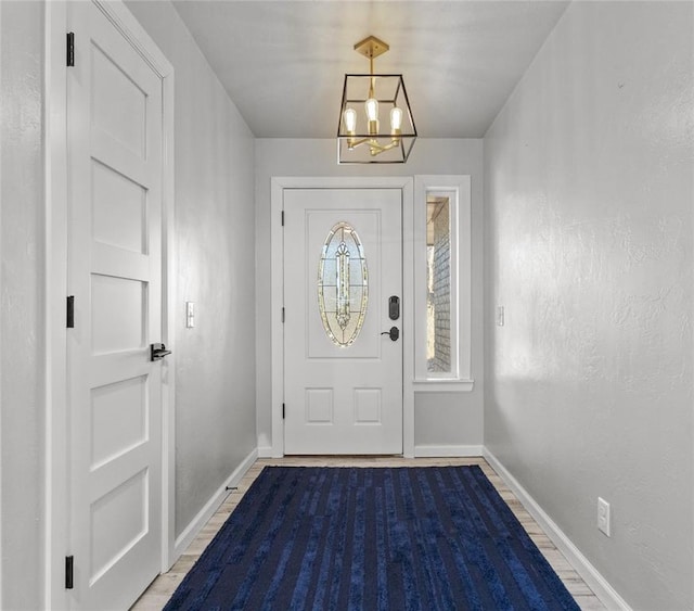 foyer entrance featuring an inviting chandelier, a textured wall, baseboards, and wood finished floors