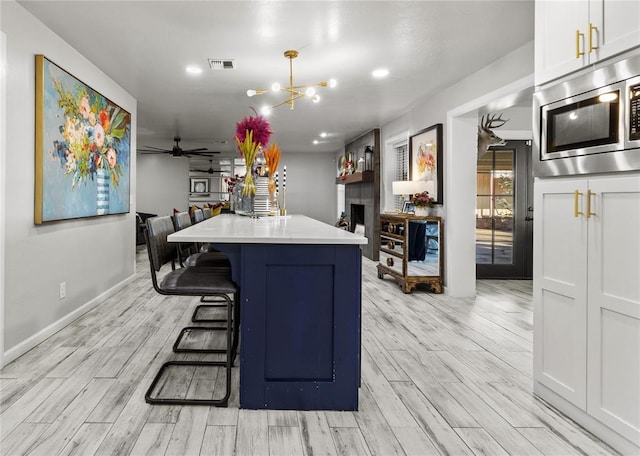 kitchen with light countertops, stainless steel microwave, visible vents, white cabinetry, and a kitchen breakfast bar