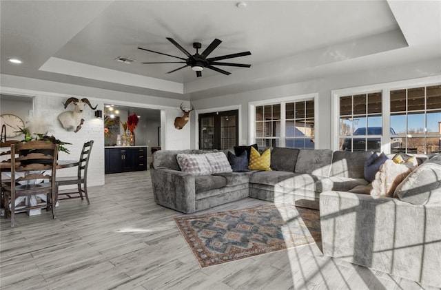 living area featuring ceiling fan, a tray ceiling, and visible vents