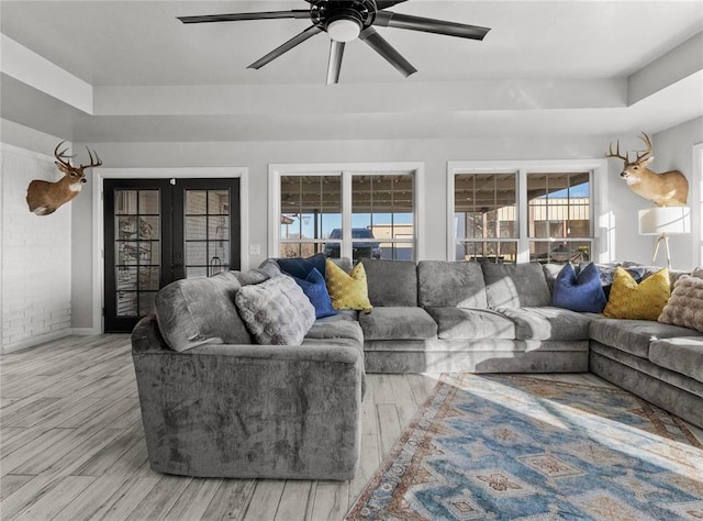 living area featuring light wood-style floors, a raised ceiling, a ceiling fan, and french doors