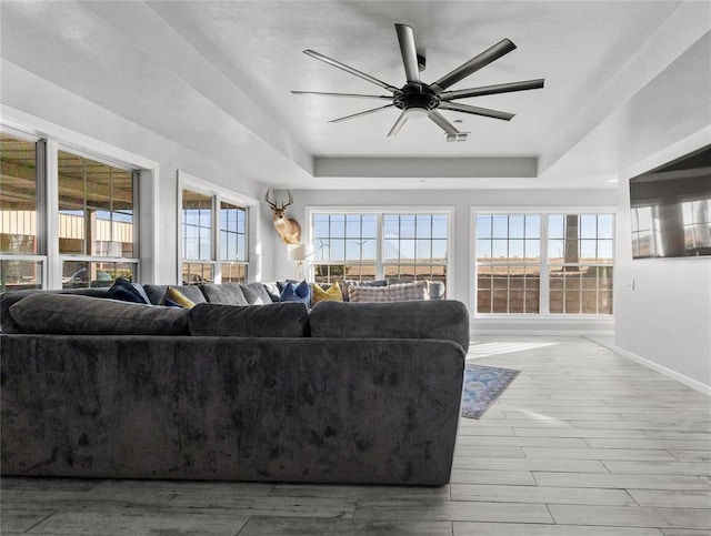 living room with a tray ceiling, visible vents, light wood-style flooring, ceiling fan, and baseboards