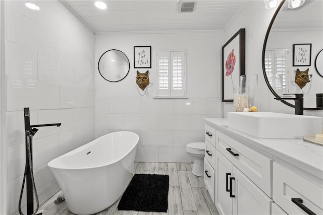 full bathroom featuring toilet, wood finished floors, a freestanding bath, vanity, and tile walls