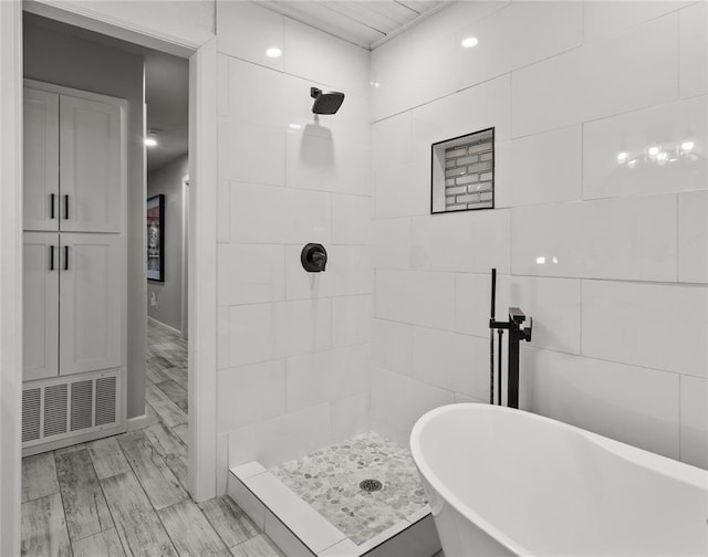 full bathroom with wood finish floors, a soaking tub, a tile shower, and visible vents