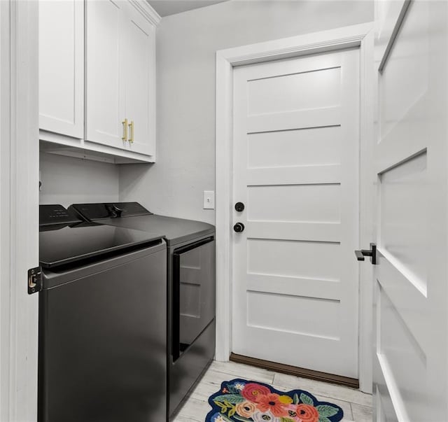 clothes washing area featuring light wood-style flooring, washing machine and clothes dryer, and cabinet space