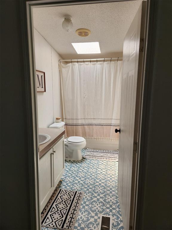 bathroom featuring toilet, a shower with curtain, a skylight, a textured ceiling, and vanity