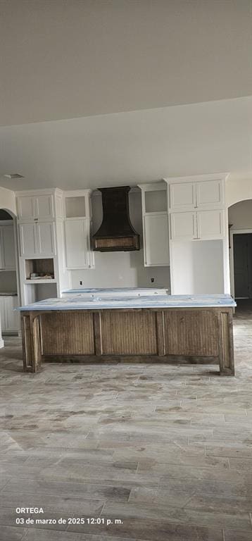 kitchen with white cabinetry, custom exhaust hood, light wood-style floors, and arched walkways