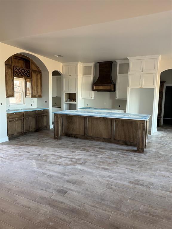 kitchen featuring white cabinetry, custom exhaust hood, light wood-style floors, and a center island