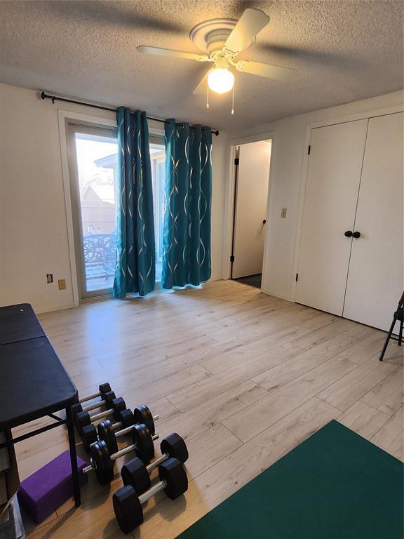 workout area featuring ceiling fan, a textured ceiling, and light wood-type flooring