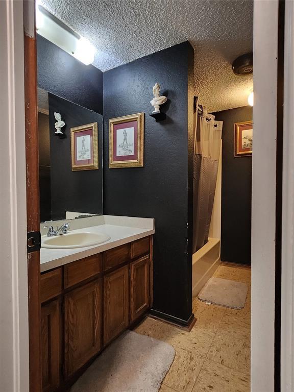 bathroom featuring shower / bath combination with curtain, vanity, and a textured ceiling