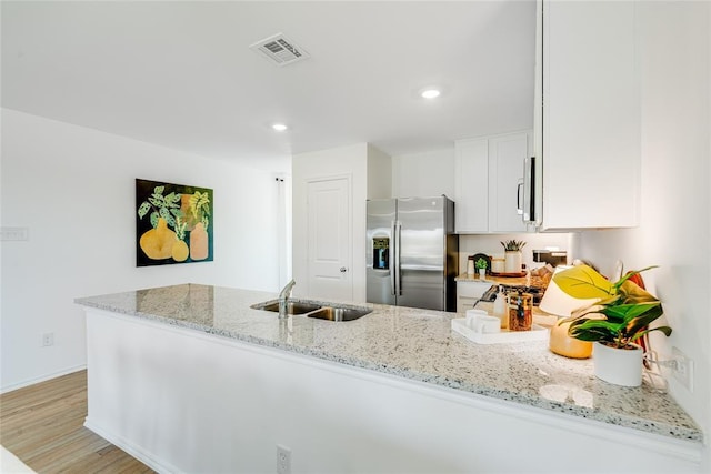 kitchen with sink, appliances with stainless steel finishes, white cabinetry, light stone counters, and kitchen peninsula