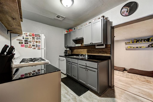 kitchen with sink, gray cabinets, white appliances, light hardwood / wood-style floors, and decorative backsplash